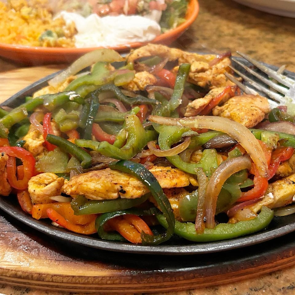 Sizzling chicken fajitas with colorful bell peppers and onions on a hot skillet at Frida's Mexican Restaurant.