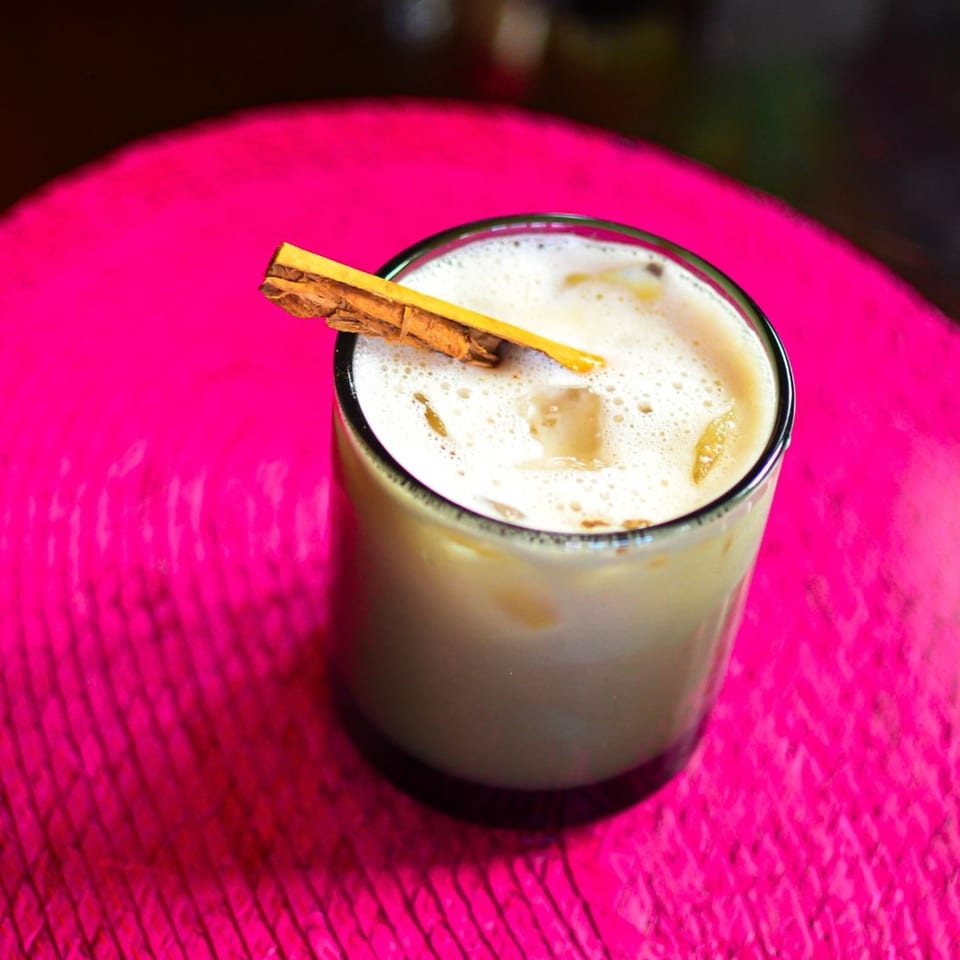 Horchata, a traditional Mexican drink, garnished with a cinnamon stick on a vibrant pink surface.